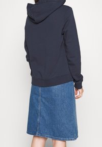 Mörkblå hetsocka med känguruficka, mjuk textur och dragsko i huvan, i kombination med en knälång blå denimkjol med en mittsöm.