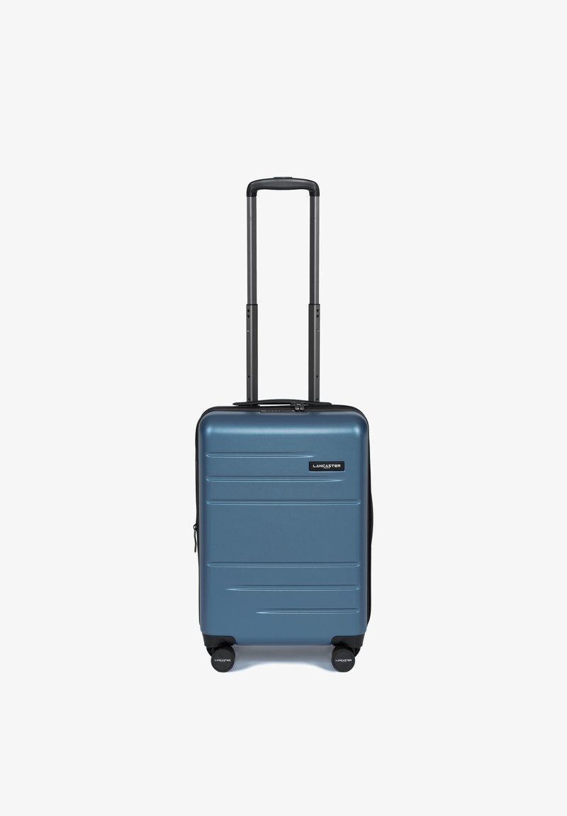 Hard-shell handbagagekoffer in een metallic blauwe afwerking, met zwarte wielen, een uitschuifbare handgreep en horizontale ribbels op het oppervlak.