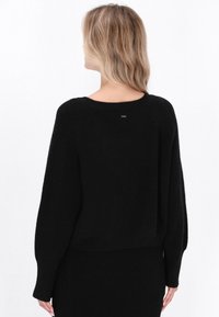 Czarny dzianinowy sweter o luźnym kroju, z prążkowaną fakturą i szerokimi rękawami. Posiada okrągły dekolt i mały detal z logo na plecach.