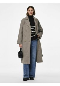 Cappotto grigio in lana doppiopetto con bottoni dorati, indossato sopra un maglione a righe bianche e nere e jeans a gamba larga, mentre tiene una borsa nera.