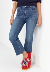 Light blue denim flared jeans with a high waist, finished with classic pockets and a subtle faded texture, paired with red sneakers.