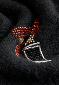 Čierna textúrovaná látka s detailnou výšivkou z korálikov v červenej, zlatej, striebornej a čiernej farbe, vytvárajúca abstraktný dekoratívny vzor.