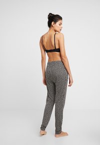 Schwarzer Bralette mit verstellbaren Trägern, kombiniert mit hochtaillierten Hosen, die ein weißes abstraktes Muster auf schwarzem Hintergrund zeigen.