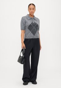 Gray short-sleeve fuzzy sweater with a large diamond pattern, paired with black wide-leg trousers and a black handbag with studded accents.