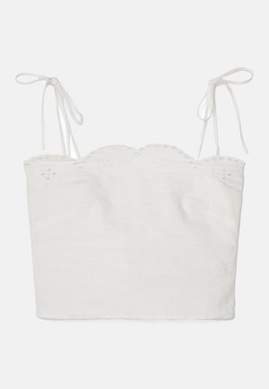 Top court blanc avec des bretelles ajustables à nouer, décolleté festonné et bordure en broderie ajourée. Fabriqué à partir d'un tissu léger.