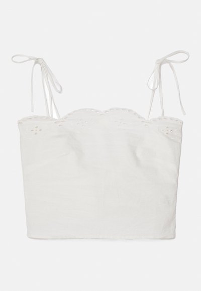 Top court blanc avec des bretelles ajustables à nouer, décolleté festonné et bordure en broderie ajourée. Fabriqué à partir d'un tissu léger.