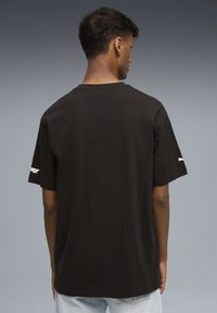 Sort bomulds T-shirt, afslappet pasform, korte ærmer, rund halsudskæring, logo accent på ærmet, glat tekstur, båret med lyse jeans.