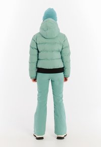 Mintgroene pufferjack met een capuchon, geribbelde zwarte zoom en bijpassende flared pants. Een gebreide lichtblauwe beanie maakt de outfit compleet.