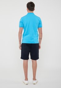 Polo shirt azzurro chiaro, maniche corte, in cotone. Abbinato a pantaloni corti blu navy con risvolti e scarpe bianche slip-on. Design semplice e casual.