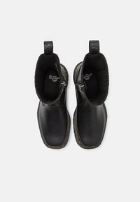 Bottes en cuir noir à cheville avec bouts carrés, fermetures éclair latérales, coutures jaunes sur les semelles et languettes avec branding sur fond blanc.