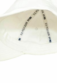Bela bejzbolska kapa z notranjim logotipom U.S. Polo Assn. Ima šivano krajko in perforacije za zračnost.