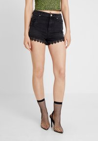 Kvinna som bär svarta slitna denimshorts med spetsdetaljer, leopardmönstrad crop top och svarta fishnet högklackade ankle boots.