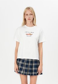 White cotton t-shirt with short sleeves and round neckline, featuring printed text and a graphic of a car. Paired with a blue plaid skirt.