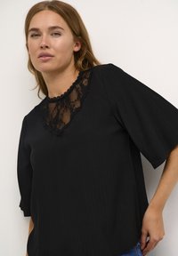 Sort bluse med en V-formet blondeudskæring, korte brede ærmer og lodret ribbet tekstur. Enkel design med fine blonde detaljer.