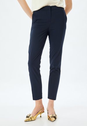 Navy blue tailored pants with a slim fit, featuring a smooth texture and a mid-rise waist, paired with gold heeled slingback shoes.