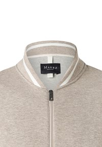 Maglione zip-up beige con colletto alzato a righe bianche e etichetta nera sul collo con la scritta "Maerz Muenchen."