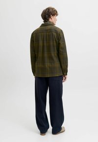 Grünes karierter Hemd mit Knöpfen aus einem weichen Stoff, im lässigen Schnitt. Kombiniert mit locker sitzenden dunkelblauen Hosen und beigen Schuhen.