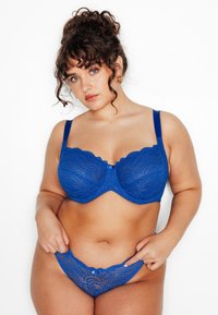 Soutien-gorge en dentelle bleue avec bords festonnés et armatures, assorti à une culotte en dentelle avec un petit nœud décoratif. Texture lisse, coupe ajustée.