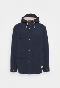 Marinblå vattentät jacka med huva, utrustad med två bröstfickor, två nedre fickor, silverknappar och krämfärgad foder.