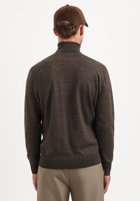 Bruin gebreid sweater met een hoge kraag, voorzien van een gladde textuur en aansluitende mouwen, gecombineerd met lichtbeige broeken.