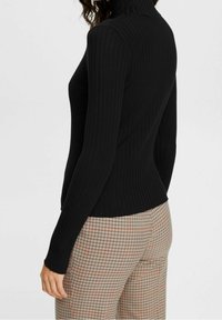 Czarny prążkowany sweter z golfem o dopasowanym kroju, zestawiony z beżowo-brązowymi spodniami w kratę z delikatnymi pomarańczowymi akcentami.