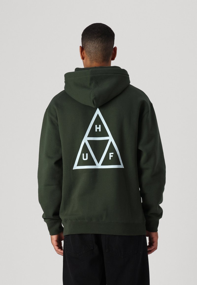 Sudadera verde oscura con un gran logo triangular blanco en la parte posterior, que presenta las letras "H", "U" y "F" dentro de los triángulos. Textura de tela suave.