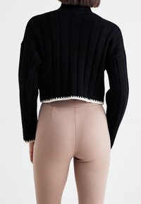 Czarny krótki sweter z pionowymi prążkami, z białą lamówką u dołu. W zestawieniu z dopasowanymi beżowymi legginsami.