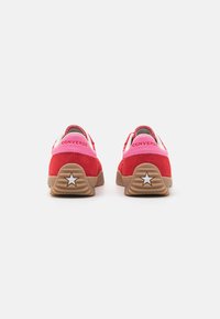 Røde ruskinds sneakers med lyserøde accenter og hvid hardware. Har en brun gummisål med en stjerne detalje på hælen. Minimalistisk design.