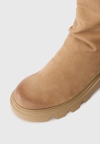 Bottine cheville en cuir tan avec une finition texturée, un bout rond et une semelle en caoutchouc épaisse avec des motifs de bandes de roulement proéminents.