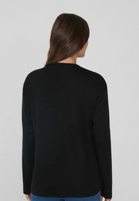 Schwarzes Langarmshirt aus weichem Stoff; verfügt über einen runden Ausschnitt und eine lockere Passform; schlichtes Design ohne Muster oder Akzente.