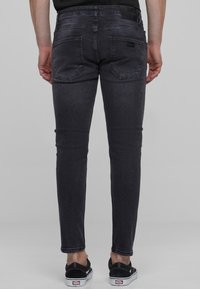 Jeans gris ajustados con un lavado sutil, que presentan dos bolsillos traseros y una etiqueta de marca en la cinturilla. Llevados con zapatillas negras.
