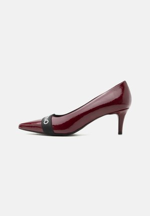 Pantof cu vârf ascuțit din piele lacuită burgundy, cu toc mediu și curea elastică neagră în față.