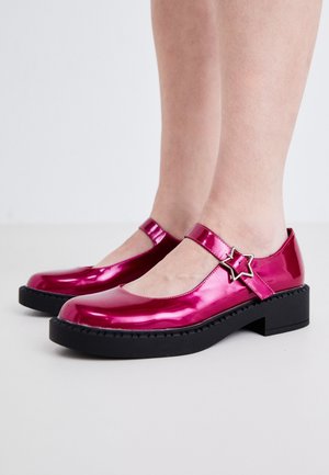 Glänzende Mary Jane Schuhe aus magentafarbenem Lackleder mit schwarzer, klobiger Sohle und sternförmiger Metallverschluss an dem Knöchelriemen.