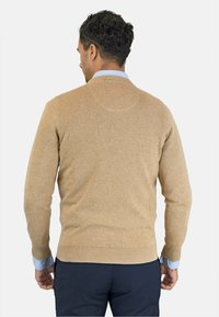 Suéter de punto beige con cuello redondo, puños y dobladillo acanalados. Llevado sobre una camisa de cuello azul claro, presenta una tela texturizada.