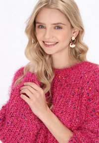 Fluffy roze sweater met kleurrijke spikkels, ronde halslijn en lange mouwen. Gouden en multispectrale kralenoorbellen. Glad, glanzend oppervlak.