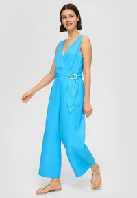 Felle blauwe mouwloze jumpsuit met een diepe V-hals, een strikband rond de taille, een wijd pijpdesign en zachte stof. Draag het met platte sandalen.