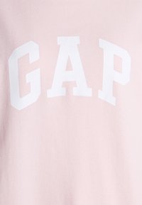 Felpa rosa chiaro con grande logo bianco "GAP"; texture liscia; scollo a giro e maniche corte. Design semplice senza ulteriori motivi.