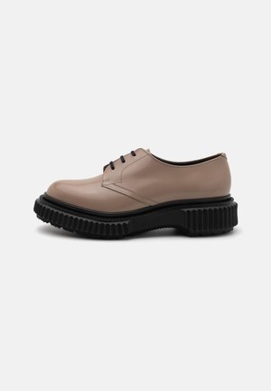 Beige Leder Schuhe mit runder Zehenpartie, schwarzer gerippter Sohle und schwarzen Schnürsenkeln. Glatte Oberfläche und minimale Nahtdetails.
