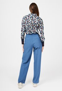 Bluse mit floralem Muster und gerafftem Rücken, kombiniert mit hellblauen weitgeschnittenen Hosen. Das Ensemble verfügt über einen Kragen und enge Manschetten.