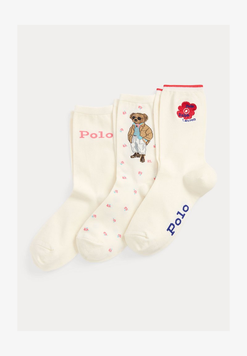 Τρεις κρεμ κάλτσες απλωμένες: μία με το "Polo" σε ροζ, μία με αρκουδάκι σε καφέ μπουφάν και μπλε πουκάμισο, μία με κόκκινο λουλούδι και μπλε κείμενο "Polo".