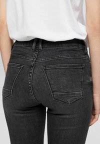 Jeans de mezclilla gris oscuro con una textura suave, que cuentan con dos bolsillos traseros y un parche de logo negro en la cintura.