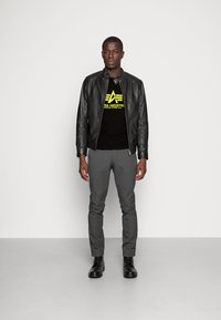 Black leather bomber jacket, black graphic t-shirt with yellow design, gray slim-fit pants, and black lace-up boots. Plain background.
