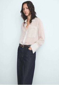 Lichte, gestreepte shirt van zachte stof met een knoopsluiting aan de voorkant, lange mouwen en een enkele borstzak. Gecombineerd met donkerblauwe wijde jeans.