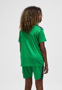 Grön sportuniform med kortärmad tröja och shorts. Materialet är slätt med svarta accenter och ett chevronmönster på sidorna.