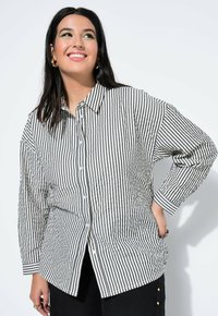 Gestreept shirt met lange mouwen met zwarte en witte verticale strepen, zachte stof, knoopsluiting aan de voorkant en een kraag.