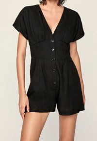 Czarny leniany kombinezon z krótkimi rękawami, głębokim dekoltem w kształcie V, zapięciem na guziki z przodu oraz kieszeniami po bokach. Gładka faktura i luźny fason.
