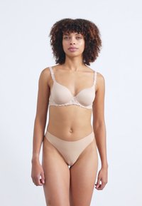 Nude pagalviniu puodeliu liemenėlė su nėriniu apdaila, reguliuojamomis petnešėlėmis ir atitinkamais bešuviais kelnaitėmis. Minkšta, lygi tekstūra su minimalistišku dizainu.