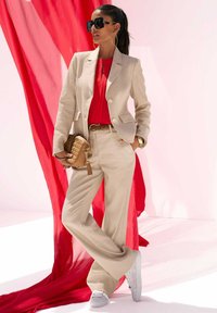 Beige pak met een fitted jas en wijde broek, gecombineerd met een levendig rode top. Geaccessoriseerd met een bruine handtas en oversized zonnebril.