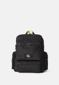 Black fabric backpack with green accent, multiple zippered pockets, and logo patch. Features textured straps and contrasting drawstring.