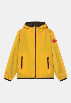 Veste en nylon jaune avec capuche, fermeture éclair sur le devant, deux poches latérales zippées et accents noirs le long de l'ourlet et des manches. Étiquette logo rouge sur la manche.